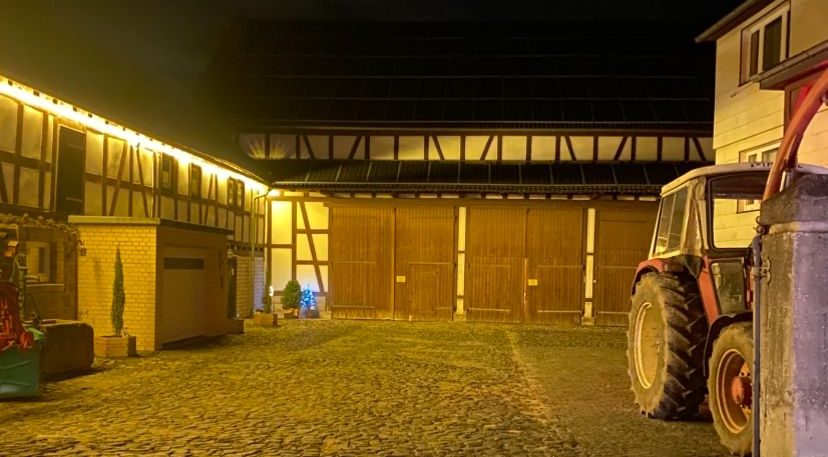 Unser Hof Scheune mit Traktor in der Nacht, beleuchtet von warmem Licht.